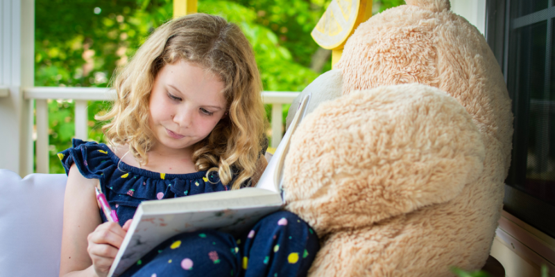 student reading her book sitting next to Extra Large stuffed animal