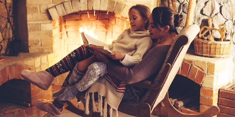 A girl reads to her mother by the fire during the holiday season