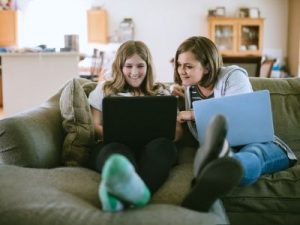 A mother and daughter do remote schoolwork next to each other on the couch