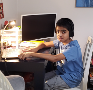 A young boy sits in front of a computer wearing headphones