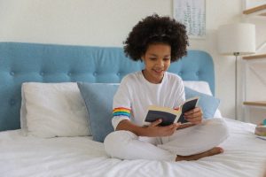 young girl sitting on bed reading a book