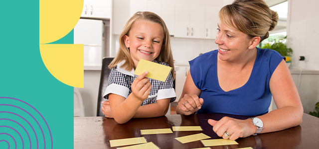 A preschool student reviews yellow flash cards on a table with her mother